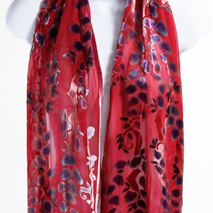 Puede incluir: Una bufanda de seda roja con un patrón floral en tonos de morado y plateado. La bufanda es transparente y tiene una sensación delicada y fluida.