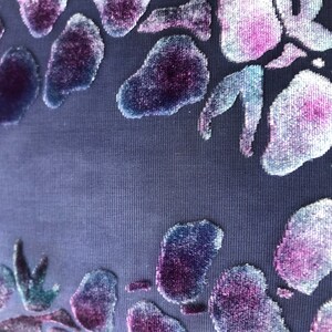 May include: A close-up of a dark blue fabric with a raised floral pattern in shades of purple, pink, and blue.