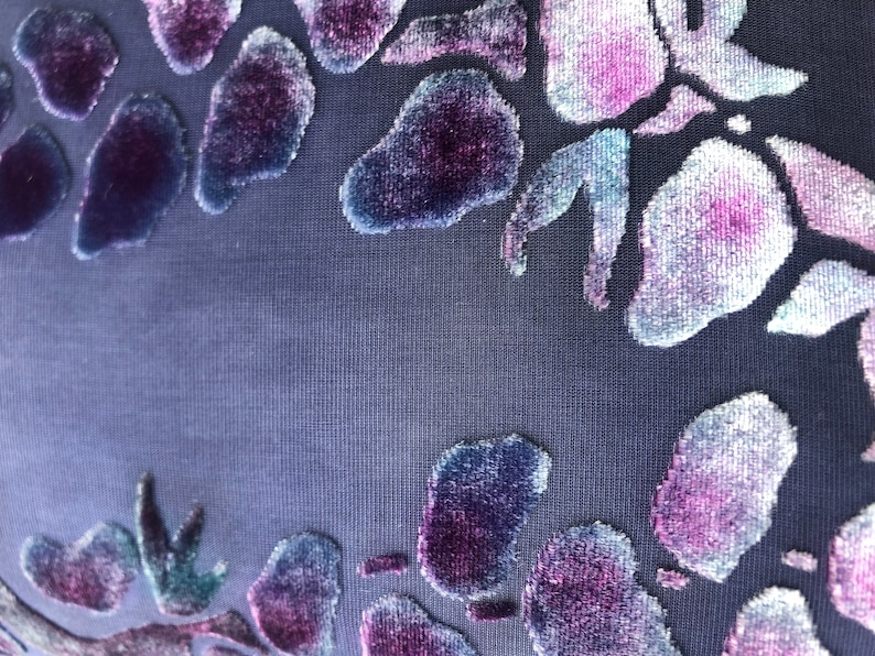 May include: A close-up of a dark blue fabric with a raised floral pattern in shades of purple, pink, and blue.