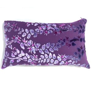 May include: A purple velvet pillow with a white floral pattern. The pillow has a subtle sheen and a soft texture.