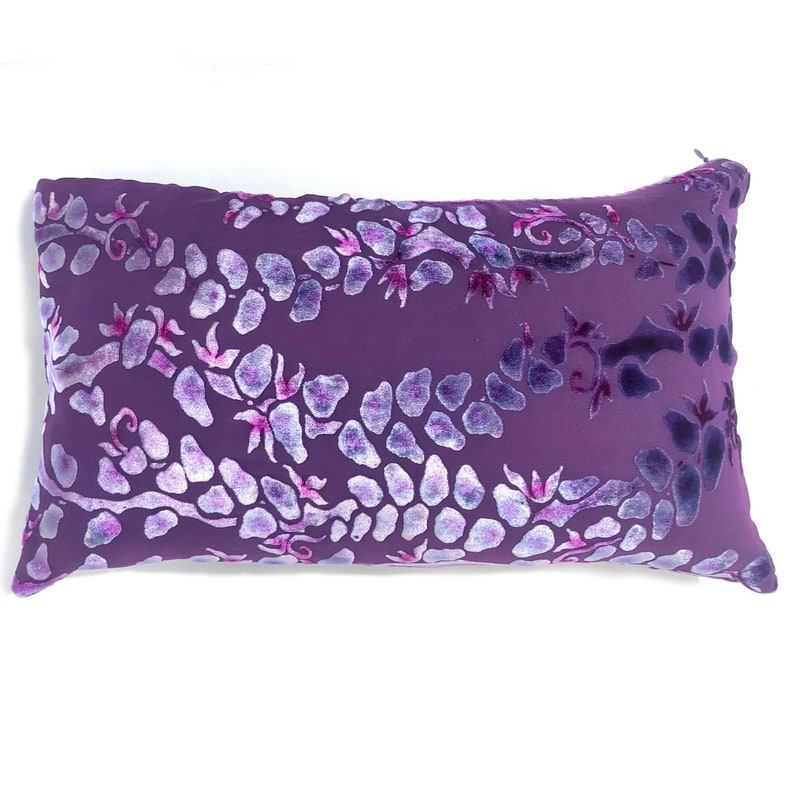 May include: A purple velvet pillow with a white floral pattern. The pillow has a subtle sheen and a soft texture.