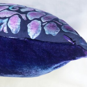 May include: A blue velvet pillow with a purple and white floral design. The pillow has a zipper closure.