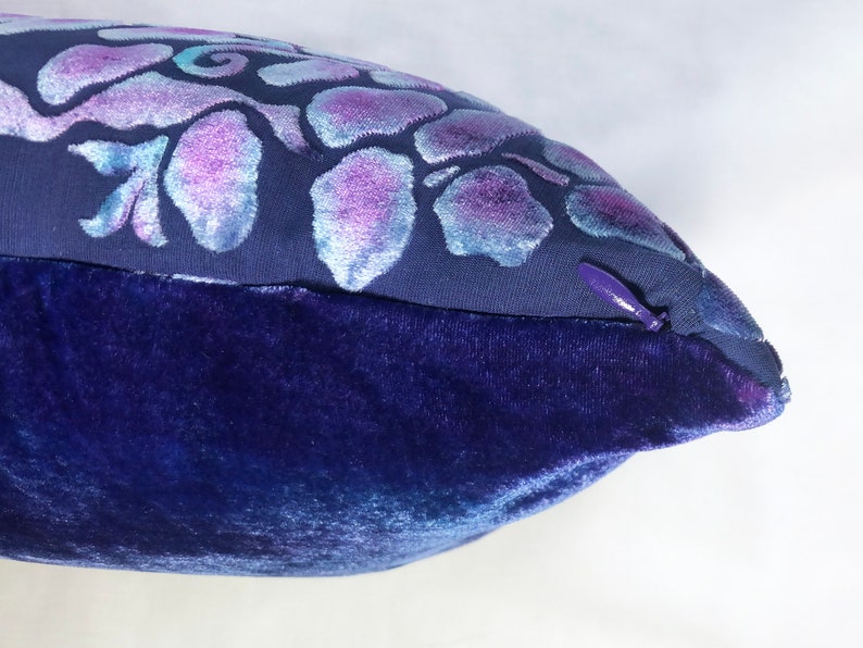 May include: A blue velvet pillow with a purple and white floral design. The pillow has a zipper closure.