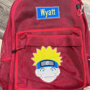 May include: A bright red mesh backpack featuring a rectangular blue patch with the name Wyatt in yellow text. Below the name, a large embroidered patch depicts a cartoon character with spiky yellow hair and a blue headband with a symbol.