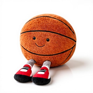 Könnte beinhalten: Ein Plüsch-Basketballspielzeug mit einem lächelnden Gesicht und schwarzen Augen. Der orangefarbene Ball hat schwarze Streifen und trägt rote und schwarze Turnschuhe mit weißen Akzenten. Das Spielzeug ist als freundlicher Charakter gestaltet.