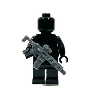 May include: A black Lego figure holding a gray rifle with a scope. The figure is a solid black color, with a smooth, glossy finish. The rifle has intricate details, including a magazine and a sight.