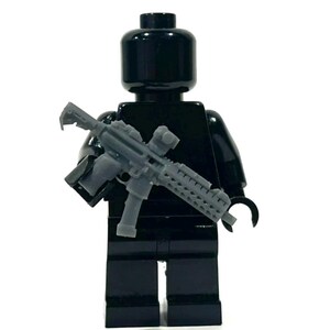 May include: A black Lego figure holding a gray rifle. The figure is entirely black, with a smooth, glossy finish. The rifle has intricate details, including a scope and a textured handguard.
