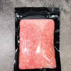 May include: A clear plastic bag filled with pink bath salts. The bag is sealed with a black zipper.
