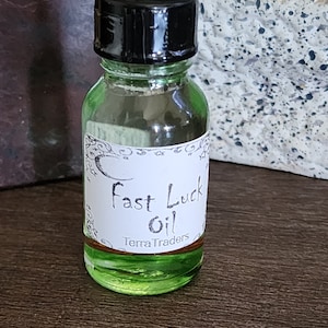 May include: A small green glass bottle with a black cap and a white label that reads "Fast Luck Oil" and "Terra Traders".