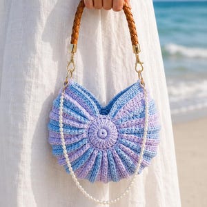 May include: A round, pleated crochet handbag featuring alternating light blue and lavender stripes. The bag includes a braided brown leather handle attached with gold-tone hardware and a decorative white pearl bead chain draped across the front.