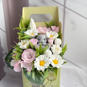 May include: A light yellow cardboard gift box containing a decorative arrangement of artificial white daisies with yellow centres, pink flowers, green leaves, and a small grey rabbit figurine. The box features the text MADE FOR LOVE at the bottom.