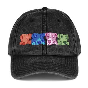 Puede incluir: Una gorra de béisbol negra con efecto lavado al ácido que presenta un estampado gráfico de cuatro cabezas de perro en fila. Los perros están coloreados en tonos sólidos de naranja, azul, rosa y verde, con ojos y orejas grandes al frente.