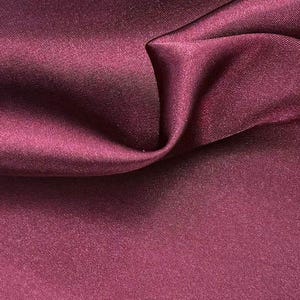 May include: A deep burgundy fabric with a smooth, satin-like finish and a subtle sheen. The material is draped to create soft, flowing folds and gentle curves, highlighting the consistent dark red color and the fine, uniform texture of the weave.