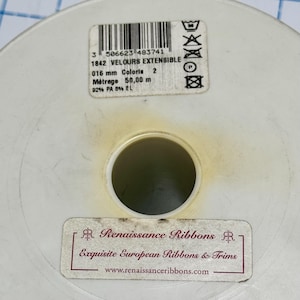 May include: A round white plastic spool for ribbon with two labels. The top label shows a barcode, 1842 VELOURS EXTENSIBLE, 016 mm, 50,00 m, and care symbols. The bottom label reads Renaissance Ribbons, Exquisite European Ribbons & Trims, and a website.