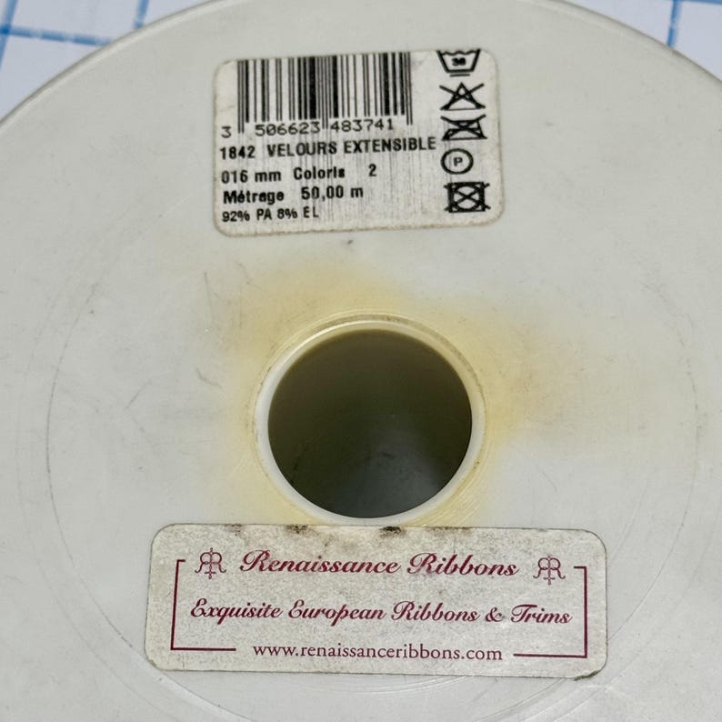 May include: A round white plastic spool for ribbon with two labels. The top label shows a barcode, 1842 VELOURS EXTENSIBLE, 016 mm, 50,00 m, and care symbols. The bottom label reads Renaissance Ribbons, Exquisite European Ribbons & Trims, and a website.