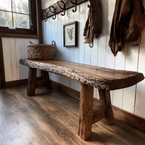 May include: A long wooden bench featuring a natural live edge top with visible bark texture and four sturdy, thick block legs. The bench is crafted from dark brown wood with a visible grain, providing a stable seating surface for an entryway.