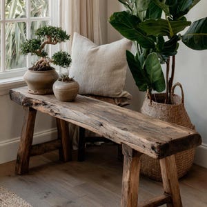 May include: A rustic wooden bench with a natural live edge, featuring four sturdy legs and a weathered brown finish. The bench is positioned horizontally, showcasing a rough, textured surface with visible wood grain and organic imperfections.