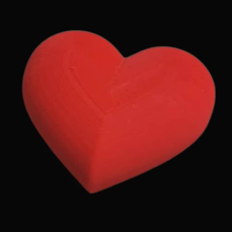 May include: A solid red heart shape against a black background. The heart is three-dimensional and has a smooth, matte finish. The image is a close-up, highlighting the heart's form and color.
