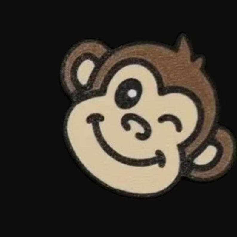 May include: A smiling monkey face with a winking eye, rendered in brown, tan, and black. The monkey's face is tan with brown outlines and ears. The background is solid black.