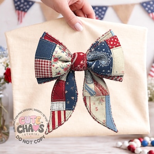 May include: A cream-colored t-shirt featuring a large, patriotic bow. The bow is made of patchwork fabric in red, white, and blue patterns, including stars, stripes, and floral designs. The text "CUTE CHAOS STUDIO" is printed on the shirt.