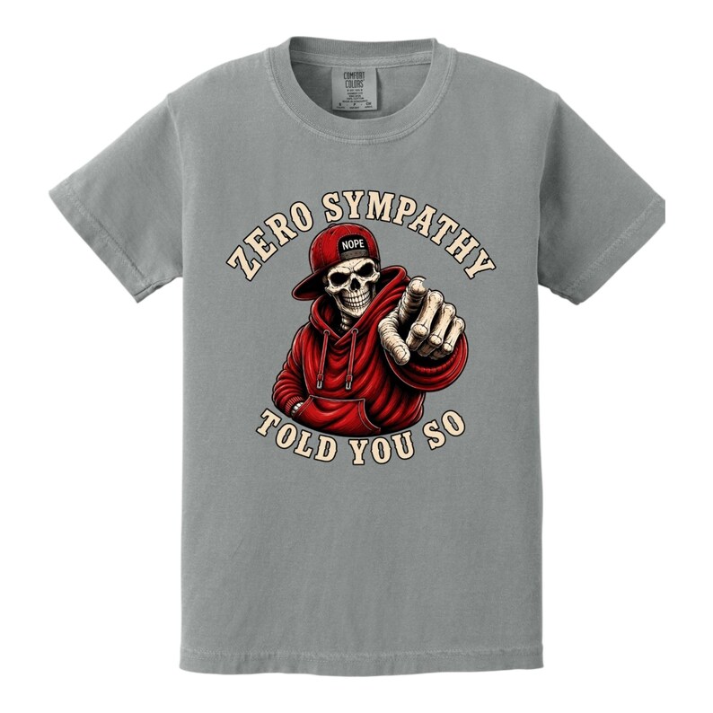 May include: Gray t-shirt featuring a graphic of a skeleton wearing a red hoodie and hat, pointing. The text reads "ZERO SYMPATHY TOLD YOU SO". The hat has the word "NOPE" on it.