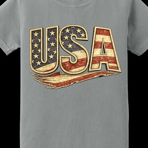 May include: Gray t-shirt with the word "USA" in a distressed design. The letters are filled with the American flag's stars and stripes. A distressed red and gold banner is below the letters.