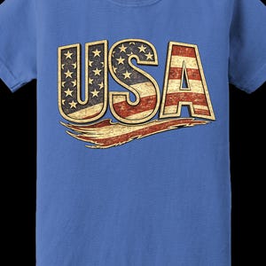 May include: Blue t-shirt with the word "USA" in a distressed, patriotic design. The letters are filled with the American flag's stars and stripes. The shirt is made of a soft material and has a classic crew neck.