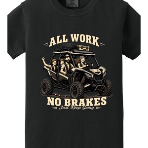May include: Black t-shirt with a graphic of a family in an off-road vehicle. The text reads "ALL WORK NO BRAKES Just Keep Going". The illustration shows a family of four in a side-by-side.