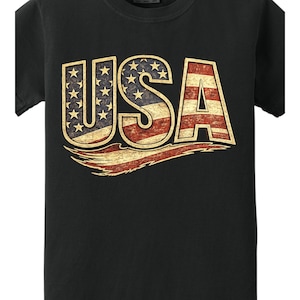 May include: Black t-shirt featuring the word "USA" in a distressed design. The letters are filled with the American flag's stars and stripes, with a vintage, worn look. The design includes a red and white banner.