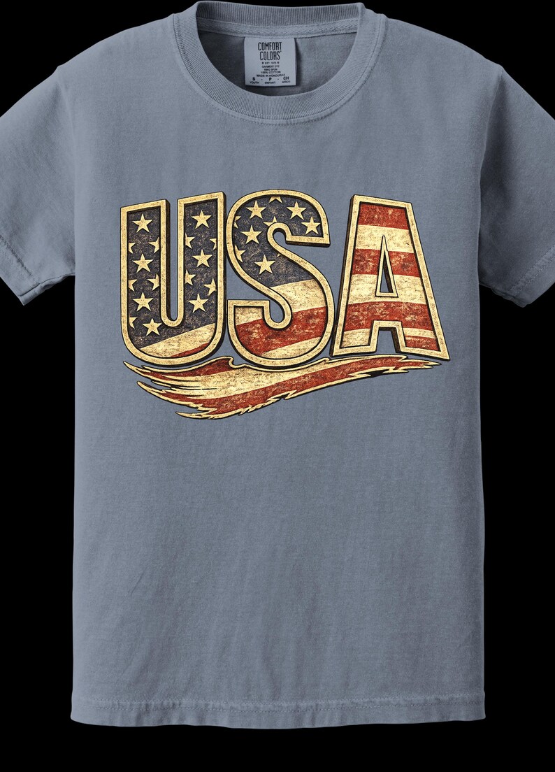 May include: A blue Comfort Colors t-shirt featuring the word "USA" in a distressed, patriotic design. The letters are filled with the American flag's stars and stripes, with a vintage, worn look.