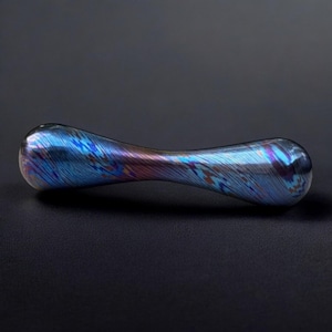 May include: A smooth, elongated, dumbbell-shaped metal object featuring a polished finish with iridescent swirls of blue, purple, and copper tones. The surface displays a fine, brushed texture that catches the light, creating a dynamic color gradient across the curved, rounded ends and the narrow center.