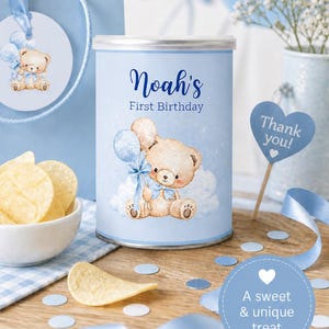 Op de afbeelding: Een lichtblauwe blik met de tekst "Noah's First Birthday", met een illustratie van een teddybeer met een ballon. De afbeelding bevat een cadeauzakje, chips en een "Thank you!"-bord, allemaal in een babyblauwe thema.