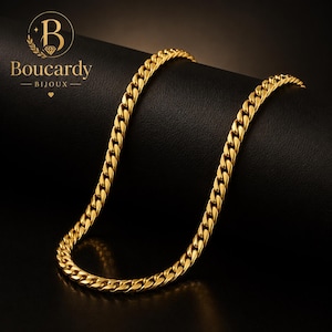 Puede incluir: Una cadena de eslabones cubanos en tono dorado con eslabones ovalados entrelazados y acabado pulido. El logotipo Boucardy BIJOUX con un icono de diamante es visible en la esquina superior izquierda sobre un fondo oscuro.