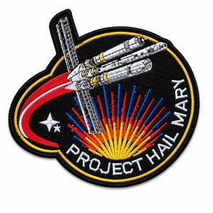 May include: Embroidered patch featuring a spacecraft design with the text "PROJECT HAIL MARY." The patch has a black background with a yellow border. The spacecraft is white and silver with yellow accents, and the design includes red, blue, and yellow streaks.