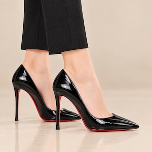 Peut inclure: Une paire d'escarpins à talons hauts en cuir verni noir avec un bout pointu et un talon aiguille fin. Les semelles des chaussures sont d'une couleur rouge vif, offrant un contraste marqué avec l'extérieur noir brillant de la chaussure.