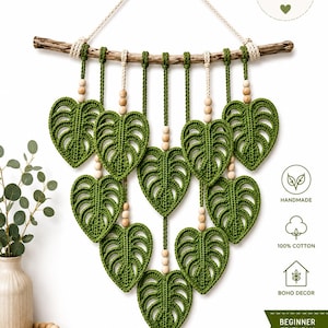 May include: A wall hanging featuring nine crocheted green monstera leaves suspended from a horizontal wooden branch. The leaves are attached with light-colored cords and wooden beads. Text on the image includes CROCHET PATTERN, HANDMADE, 100% COTTON, BOHO DECOR, and BEGINNER FRIENDLY.