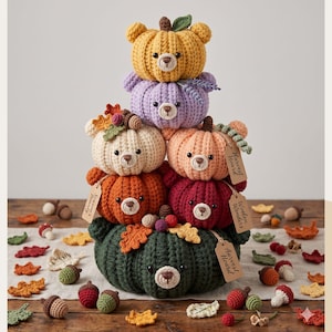 May include: A stack of handmade crochet bears shaped like pumpkins in various colors: yellow, purple, cream, orange, and burgundy. The bears have brown noses and are adorned with leaves and tags. Decorative fall leaves and acorns surround the stack.