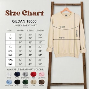 Puede incluir: Una sudadera unisex Gildan 18000 beige cuelga de una escalera de madera, con una tabla de tallas y opciones de color. La tabla enumera las tallas S a 5XL, con medidas en cm para ancho, manga y largo. Los colores disponibles incluyen blanco, azul marino, gris deportivo, rojo y rosa claro.