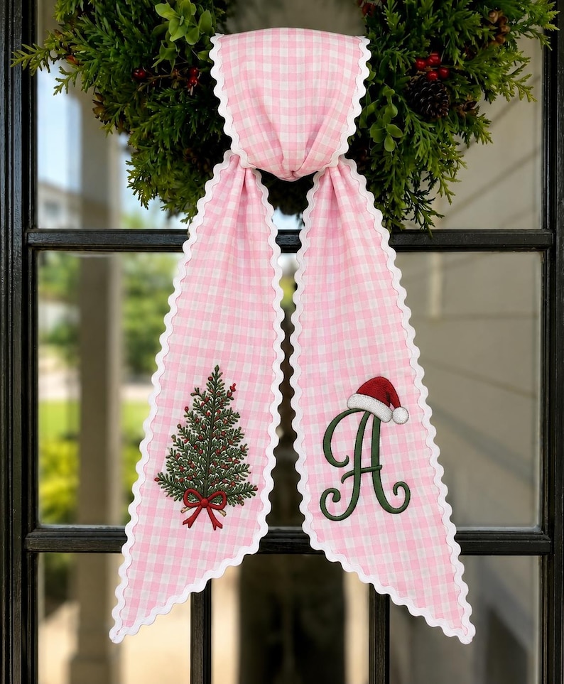 May include: A pink and white gingham fabric ribbon with scalloped white edges. The ribbon features an embroidered green Christmas tree with a red bow on the left tail and a large green letter A wearing a red and white Santa hat on the right tail.