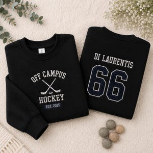 Puede incluir: Dos sudaderas negras. Una presenta "OFF CAMPUS HOCKEY" con palos de hockey cruzados y "EST. 2015" en blanco. La otra tiene "DI LAURENTIS" y el n&uacute;mero "66" en azul marino.