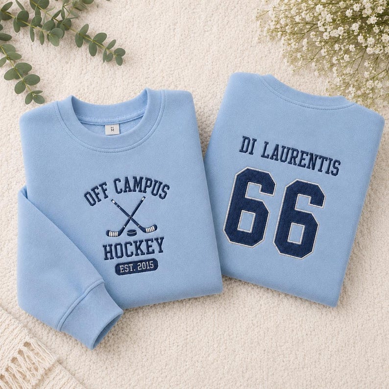 Puede incluir: Dos sudaderas azul claro. Una presenta "OFF CAMPUS HOCKEY EST. 2015" con palos de hockey cruzados. La otra tiene "DI LAURENTIS 66" en azul marino. Ambas tienen cuello redondo.