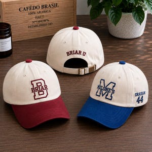 May include: Three baseball caps with different designs. One has a maroon brim and the word "BRIAR" in maroon. Another has a blue brim with "MELONE'S" and "GRAHAM 44" in blue. The third cap has "BRIAR U" on the back.