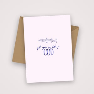 May include: A greeting card with a pale pink background and a brown envelope. The card features a blue illustration of a fish and the text "got you a bday COD".