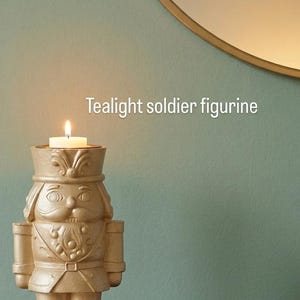 May include: Gold-colored teacup candle holder in the shape of a toy soldier. The candle holder has a lit candle inside. The text "Tealight soldier figurine" is displayed on the image.