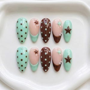 May include: A set of ten almond-shaped press-on nails featuring a mix of mint green and chocolate brown colors. The designs include polka dots, French tips, and raised star accents, complemented by small white pearl-like embellishments.