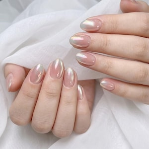 May include: Oval-shaped fingernails featuring a sheer, pale pink base coat with a pearlescent, iridescent finish that reflects subtle hints of blue and green light. The nails are groomed to a smooth, rounded edge, showcasing a glossy, reflective surface.