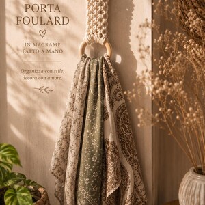 May include: A macrame scarf holder with wooden rings, holding three patterned scarves. The scarves feature floral and paisley designs in beige, green, and brown. The text "PORTA FOULARD" and "IN MACRAME FATTO A MANO" are visible.