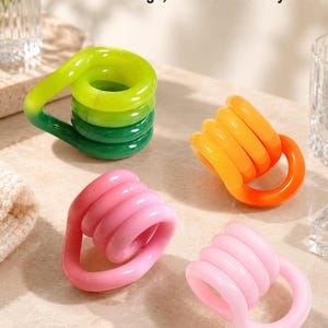 May include: Four plastic coil-shaped fidget toys in lime green, orange, and two shades of pink. The toys feature a continuous loop design. The text "Portable Storage, Stress Relief Anytime" is visible at the top of the image.