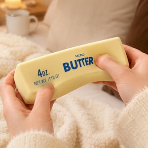 Peut inclure: Un objet rectangulaire de couleur jaune pâle en forme de beurre avec du texte bleu indiquant SALTED BUTTER, 4oz. et NET WT. (113 G). L'objet a une surface lisse et solide et est tenu entre deux mains, montrant sa structure ferme.