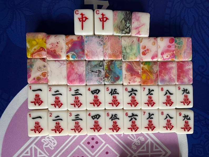 May include: A collection of white Mahjong tiles with red Chinese characters and colorful abstract designs. The tiles are arranged in rows, displaying various suits and numbers. The top row features the "C" and "中" tiles.